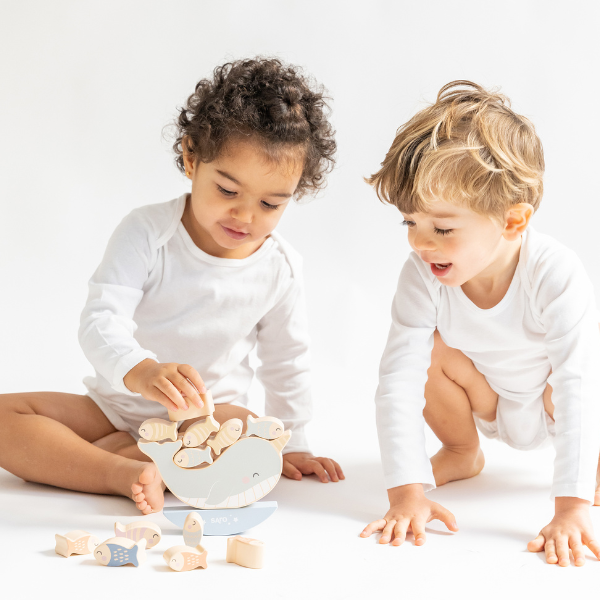 Two children playing with wooden toys on a white surface