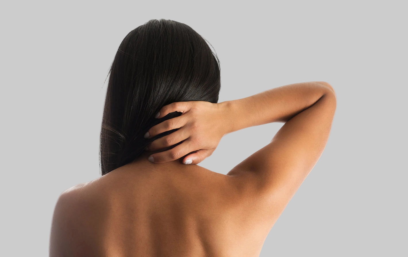 Person with long black hair touching their neck against a light background